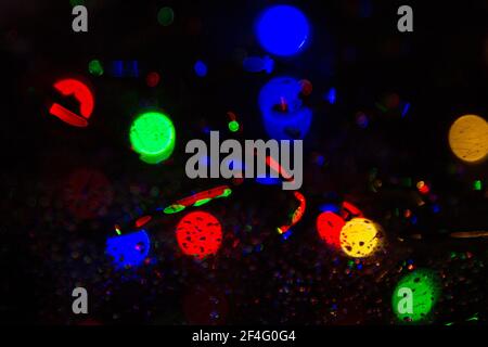 Colorful bokeh lights on a dark background behind the raindrops on the glass texture Stock Photo