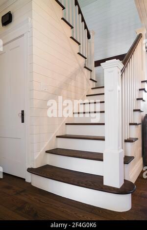 Main wooden staircase painted white with dark stained oak wood steps and handrail inside country style home Stock Photo