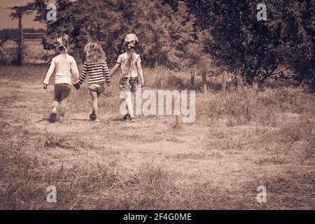 Three little girls walking outdoors holding hands. Girlfriends or sisters. Childhood. Friendship. Kids playing outside summer. Black and white photo. Stock Photo