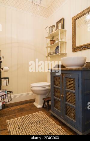 White porcelain bowl sink on top of antique blue painted pine wood pie safe cabinet,  vintage wall shelf unit with decorative objects in water closet Stock Photo