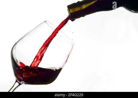 red  wine poured from a bottle into wine glass on white background, isolated Stock Photo