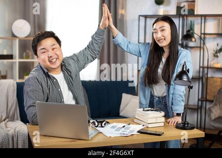Positive male and female IT specialists giving high five, smiling and looking at camera. Asian workers having successful meeting at bright office. Stock Photo