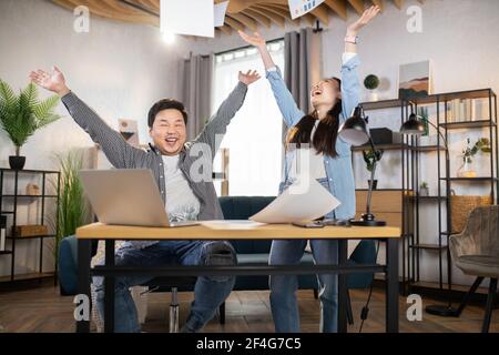 Cheerful asian young man and woman, throwing papers around after successful business meeting. Happy students celebrating exam pass. Business, education, distance learning concept. Stock Photo