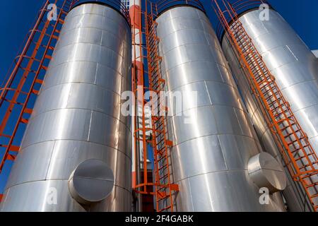 Oil Refinery Exterior with Oil Storage Tanks Over Blue Sky Background. Industrial Storage Tanks and Chimney Against the Blue Sky. Low Angle View. Stock Photo
