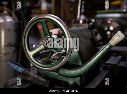 Old green lathe machine detail in the workshop. Controller wheel with handle. Selective focus. Stock Photo