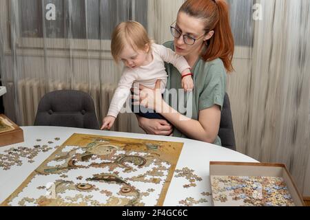 Young woman solving a puzzle in a quarantine with a daughter. Stock Photo