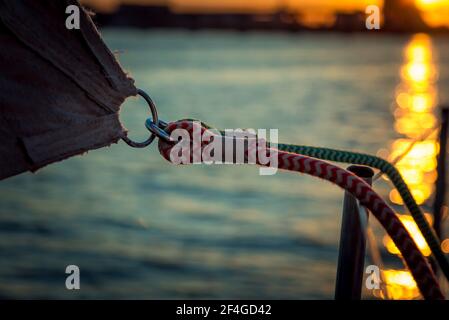 Detail of fastening the sail on a yacht in the rays of the sunset. Shooting on board a yacht on the river. Stock Photo
