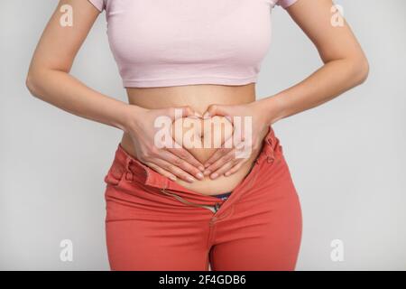 Love your body positive woman. Cropped studio shot of a woman holding her hands in a shape of heart on her fatty stomach. Stock Photo