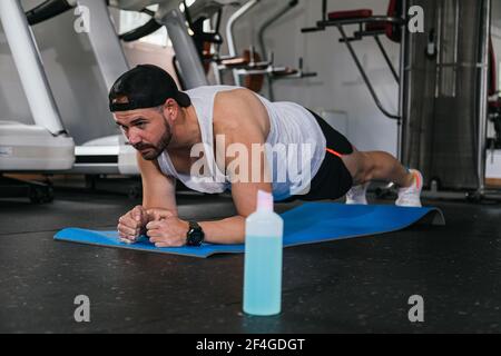 Man doing planks in the gym. Hydro alcoholic gel, coronavirus, pandemic. Stock Photo
