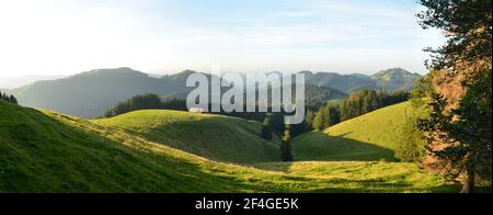 swiss hill landscape at sunset. The last rays of sun light up the meadows. Panorama in backcountry. Summer time, hiking  Stock Photo