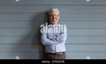 Smiling mature hoary man in glasses standing by planked wall Stock Photo