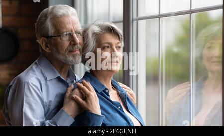 Elderly spouses hug look at window meet twilight years together Stock Photo