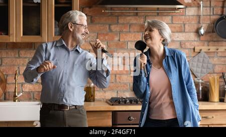 Overjoyed older senior couple having fun sing songs at kitchen Stock Photo