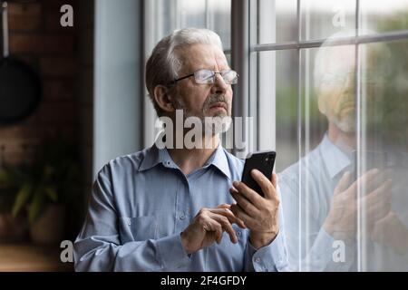 Worried older man look at window hold phone make call Stock Photo