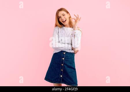 Cheerful happy young woman winking, smiling and showing ok sign, good choice, on pink background Stock Photo