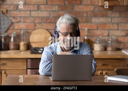 Happy aged male in headset talk by videocall on laptop Stock Photo
