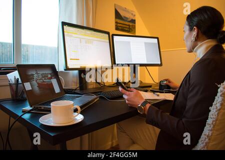 Woman Working From Home In Her Home Office With Coffee - Multiple Monitor workstation Stock Photo