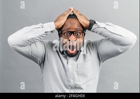 Portrait of forgetful young African American customer or employee wearing shirt looking with shocked and guilty expression, holding hands on his head, opening mouth widely, body language, Oh no Stock Photo