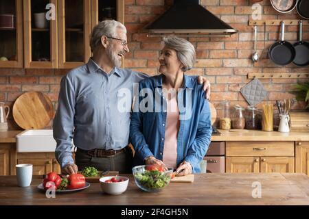 Loving mature couple vegans talk laugh cook food at kitchen Stock Photo