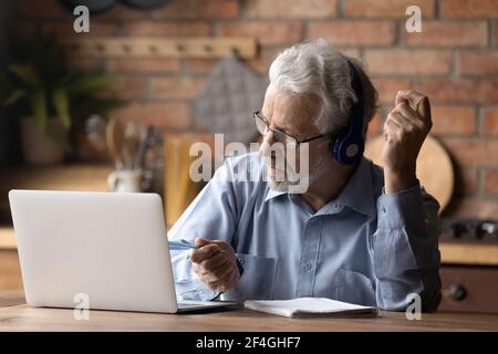 Old man in headphones watch training on laptop take notes Stock Photo
