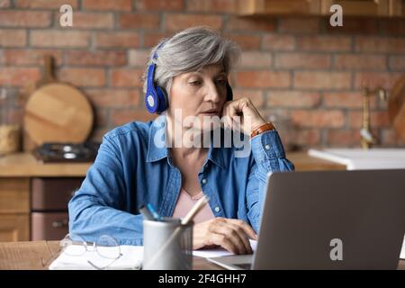 Active latin female retiree in headset confer online using laptop Stock Photo