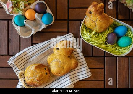 Sweet brioche dough in the shape of Easter bunnies, a basket with edible Easter grass and colored Easter eggs. Stock Photo