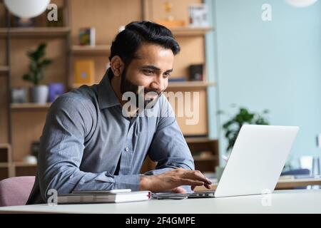 Smiling indian business man working studying on laptop computer at home office. Stock Photo