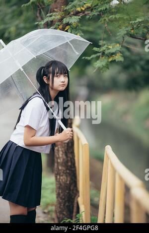 Portrait of Asian school girl walking with umbrella at nature walkway on raining Stock Photo