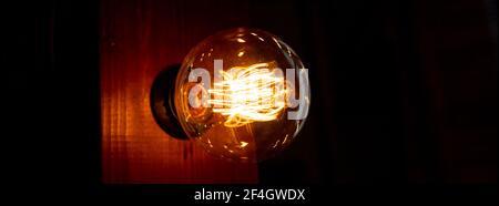 Old glowing light bulbs on dark background.Bright glowing clear glass lamp pear shaped close up.Lighting decoration.web banner Stock Photo
