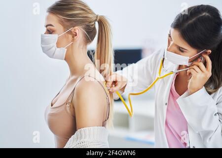 Doctor in mask checking up on female patient using stethoscope Stock Photo