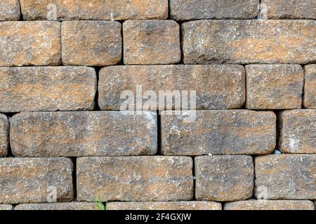 A stone wall made of old yellow bricks. No mortar was used between the bricks. Sunny day, closeup view. Stock Photo