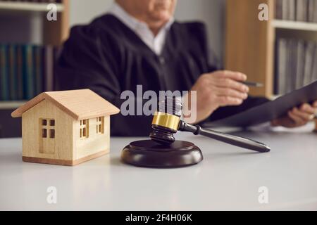 Closeup of judge's gavel and little wooden toy house placed on table in court of law