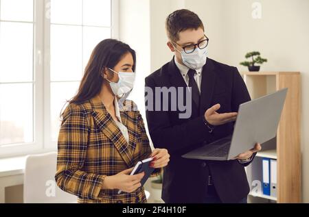 Office workers in medical face masks working on business project and using laptop Stock Photo
