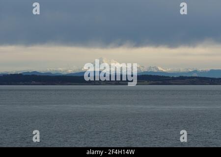 View on snow covered mountain form merchant vessel approaching Vancouver, British Columbia  from Pacific ocean under heavy rainfall clouds. Stock Photo