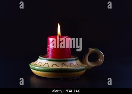 A lit red candle in a yellow and green ceramic candlestick. Cocept of hope, mourning or prayer. Stock Photo