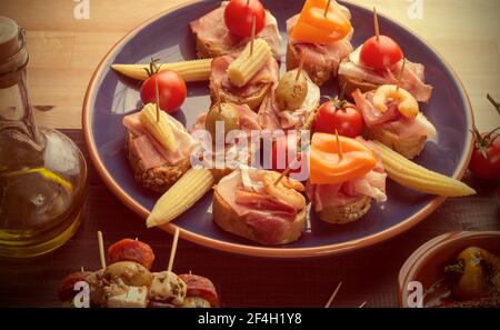 Variety of Mediterranean snacks on blue plate. Tapas or antipasti. Vintage effect Stock Photo