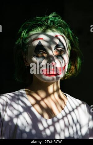 Thoughtful young woman with a body art as joker clown on dark black background. Stock Photo