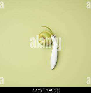 plastic knife for peeling vegetables, fruits and a green apple on a green background, top view Stock Photo