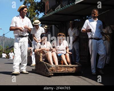 Madeira, Portugal. 09,05,2017 Couple of tourists starting down the slopes of the streets of Funchal in wicker baskets or 'carros do cestos'. Stock Photo