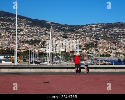 Madeira, Portugal. 09,05,2017     Retired tourist couple in the harbour of Funchal with the town houses in the background on a sunny summer day. Stock Photo