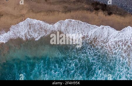 overhead shot of a couple on a beach walking on the shore with wave reaching Stock Photo