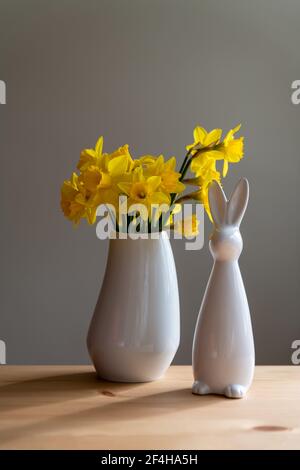 Beautiful Easter and spring decorations. Idea for a coherent interior design. Daffodils and a white Easter bunny in white porcelain. Portrait format. Stock Photo