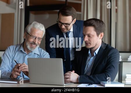 Smiling male colleagues cooperate at laptop discussing ideas Stock Photo