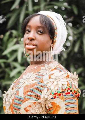 Side view of young African female in kerchief looking at camera against plant in summer Stock Photo