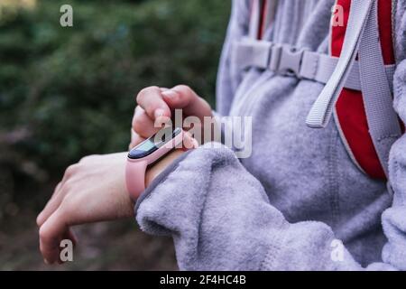 Side view of crop female in activewear with backpack using GPS on fitness tracker for navigation during hiking in forest Stock Photo