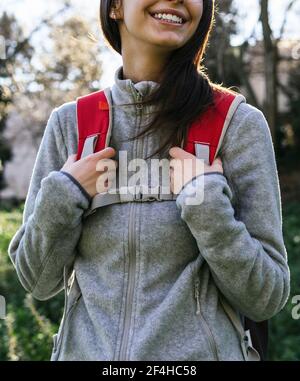 Anonymous happy optimistic young female hiker in activewear with backpack enjoying journey in green forest in sunny day Stock Photo