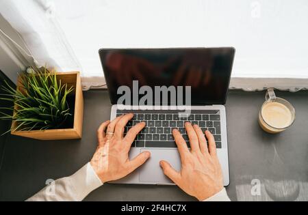 From above cropped unrecognizable middle aged male working on counter with netbook and cup of coffee in kitchen in the morning Stock Photo