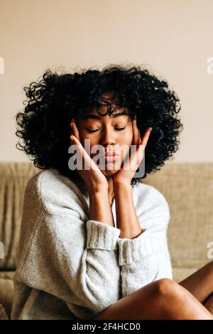 Gentle African American female in sweater and with Afro hairstyle showing duck face with closed eyes at home Stock Photo
