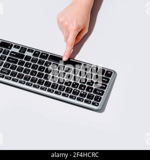 From above anonymous person pushing button on computer keyboard on gray background Stock Photo