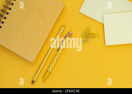 Top view composition with yellow notebook and pens placed near blank sticky notes and paper clips on yellow background Stock Photo